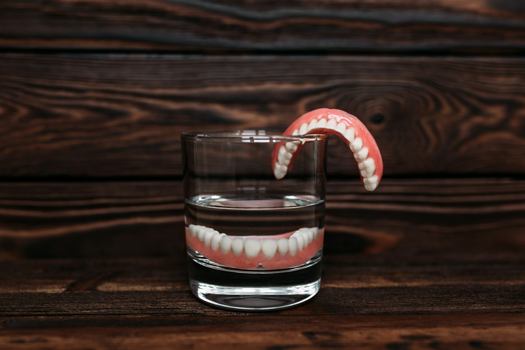 A denture in a glass of water. Dental prosthesis care. Full removable plastic denture of the jaws